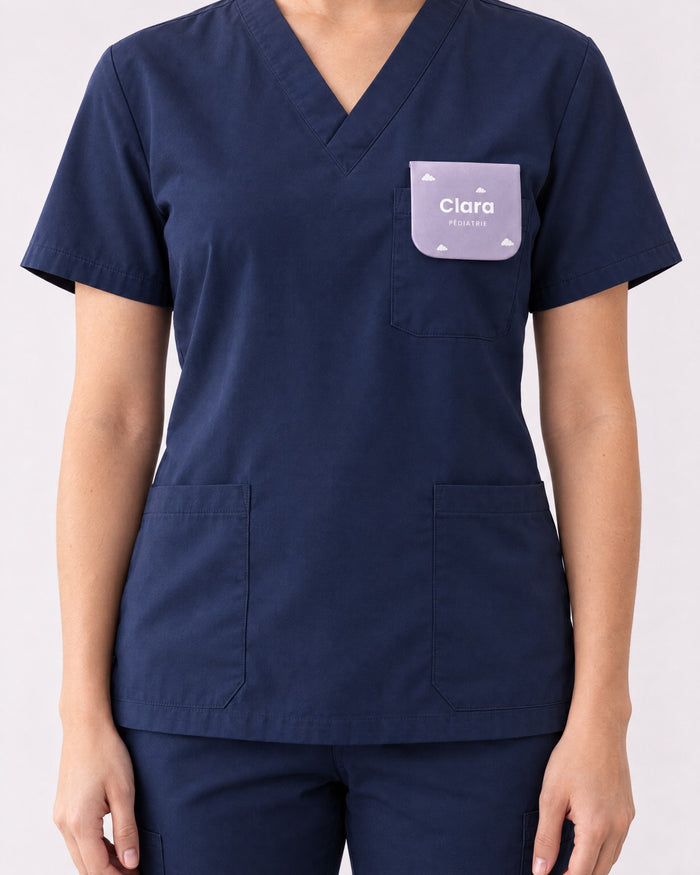 Pochette personnalisée « Clara · Pédiatrie » portée dans la poche poitrine d'une blouse bleu marine